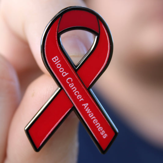 Red ribbon with 'Blood Cancer Awareness' text held in a hand against a blurred background