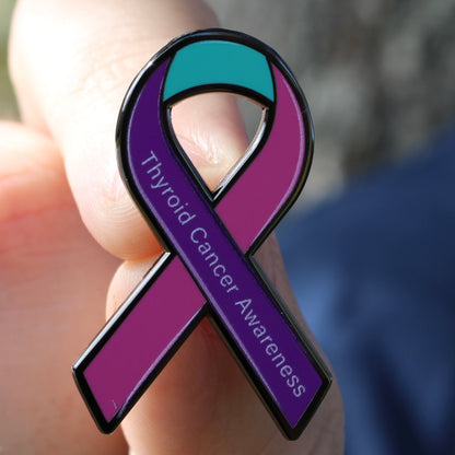 Purple thyroid cancer awareness ribbon pin held in a hand with a blurred background
