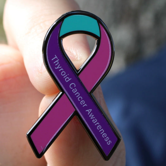 Purple thyroid cancer awareness ribbon pin held in a hand with a blurred background