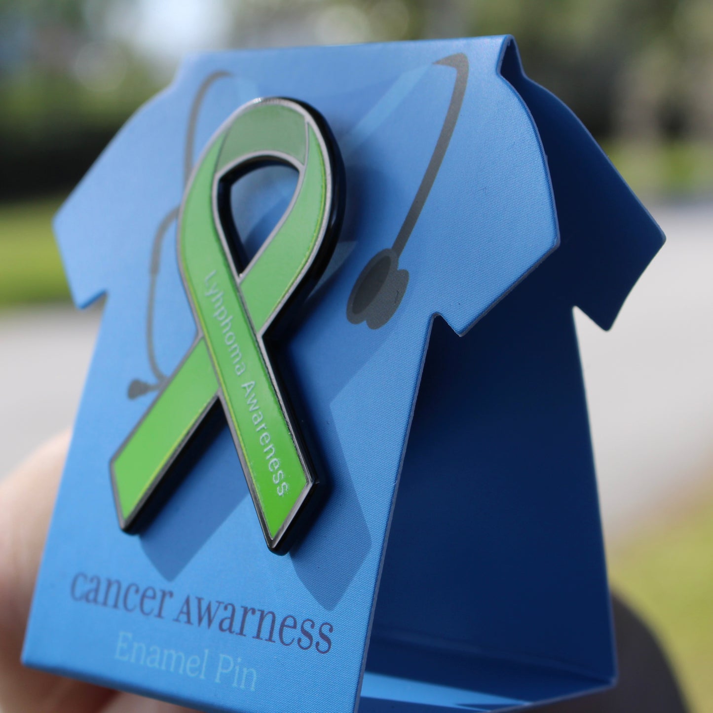 Green ribbon cancer awareness enamel pin on a blue card