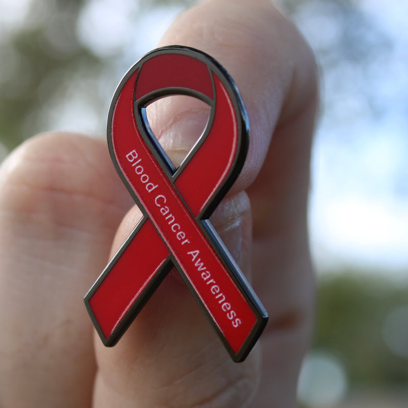 Red ribbon with 'Blood Cancer Awareness' text held in a hand against a blurred natural background