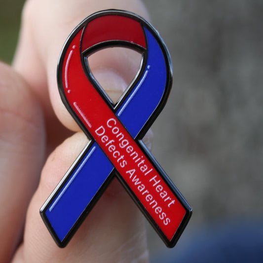 congenital heart defects Red and blue awareness ribbon pin held in a hand with a blurred background