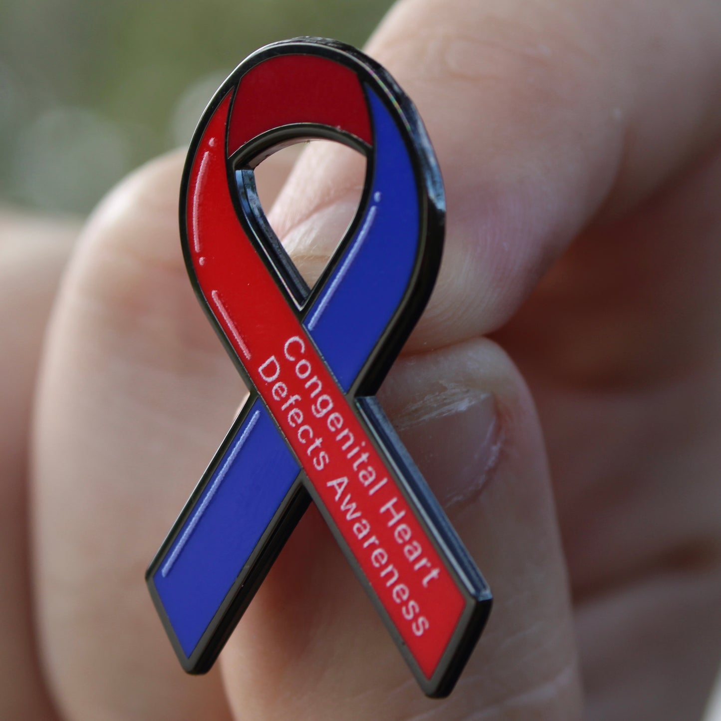 Red and blue awareness ribbon pin held in a hand with 'Congenital Heart Defects Awareness' text.