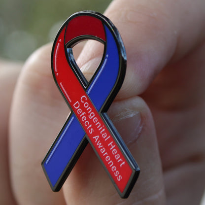 Red and blue awareness ribbon pin held in a hand with 'Congenital Heart Defects Awareness' text.