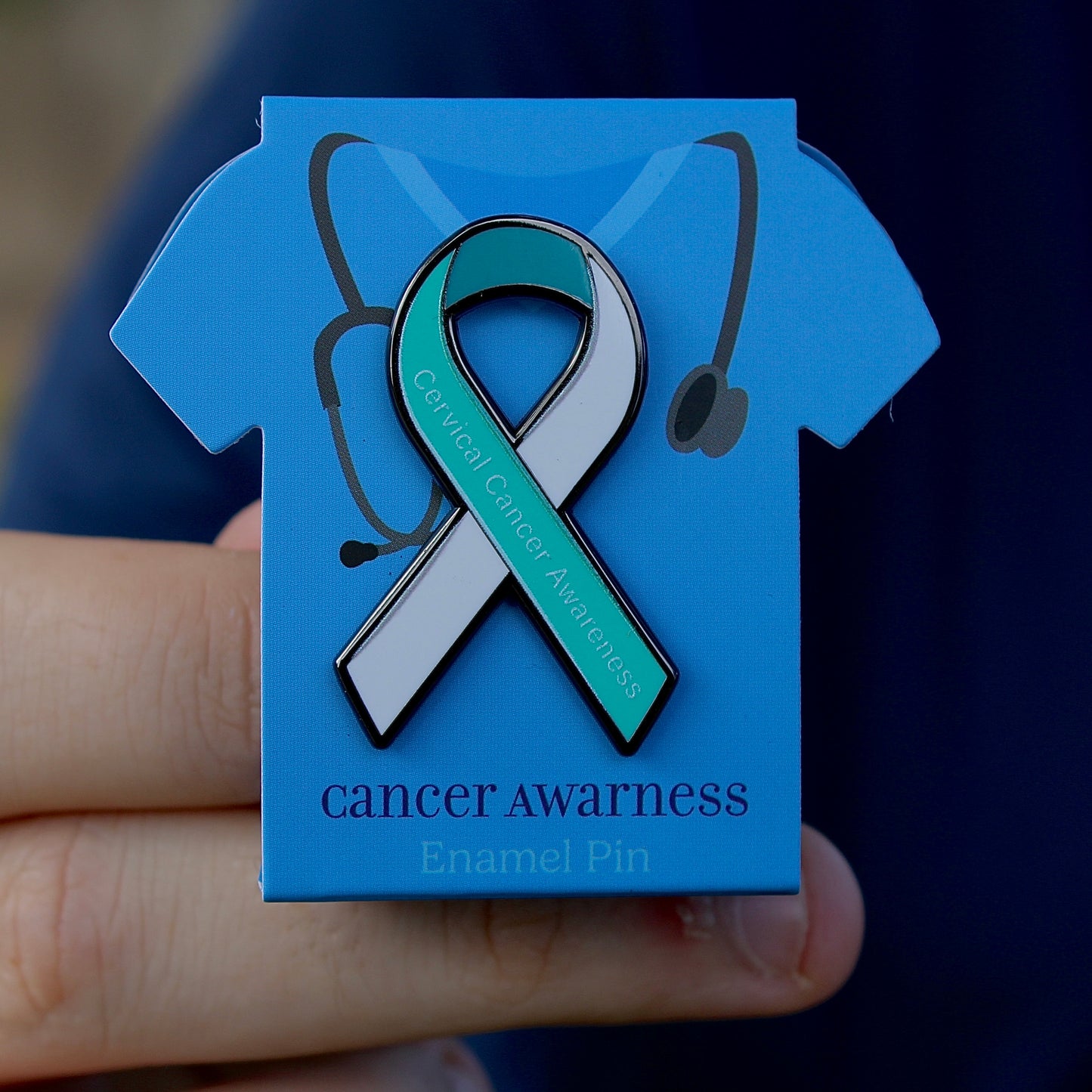 Cervical cancer awareness teal and white ribbon pin on blue scrub display stand