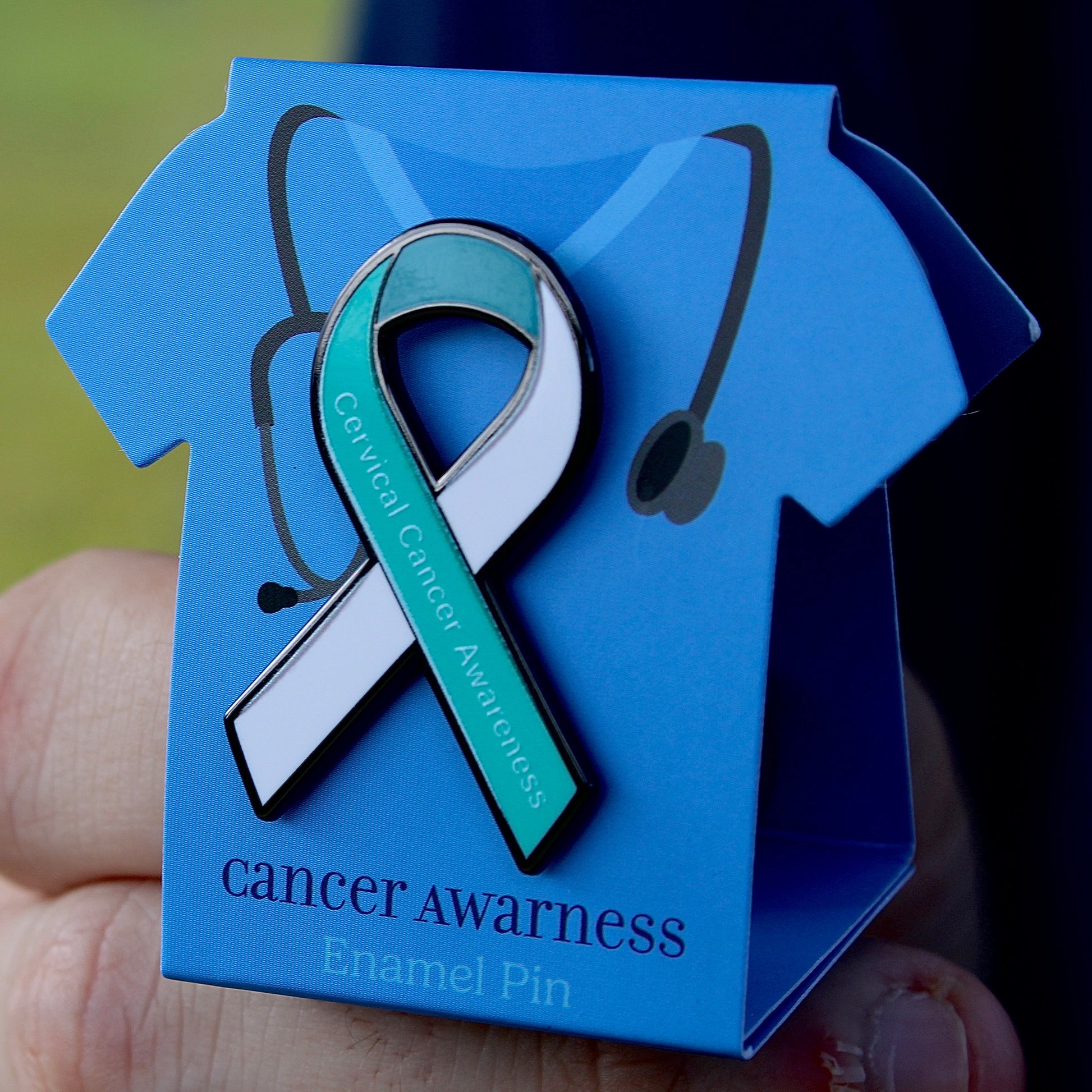 Cervical cancer awareness enamel pin in a blue scrubs display box held by a hand.