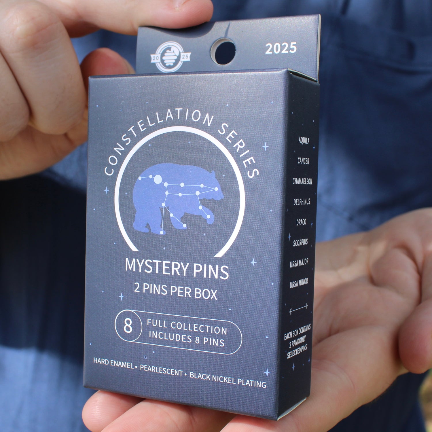 Box of Constellation Series Mystery Pins held by a person