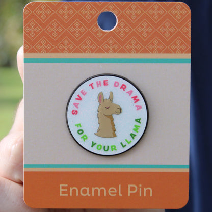 Enamel pin with font "save the drama for your llama" and a llama design on a card held by a hand