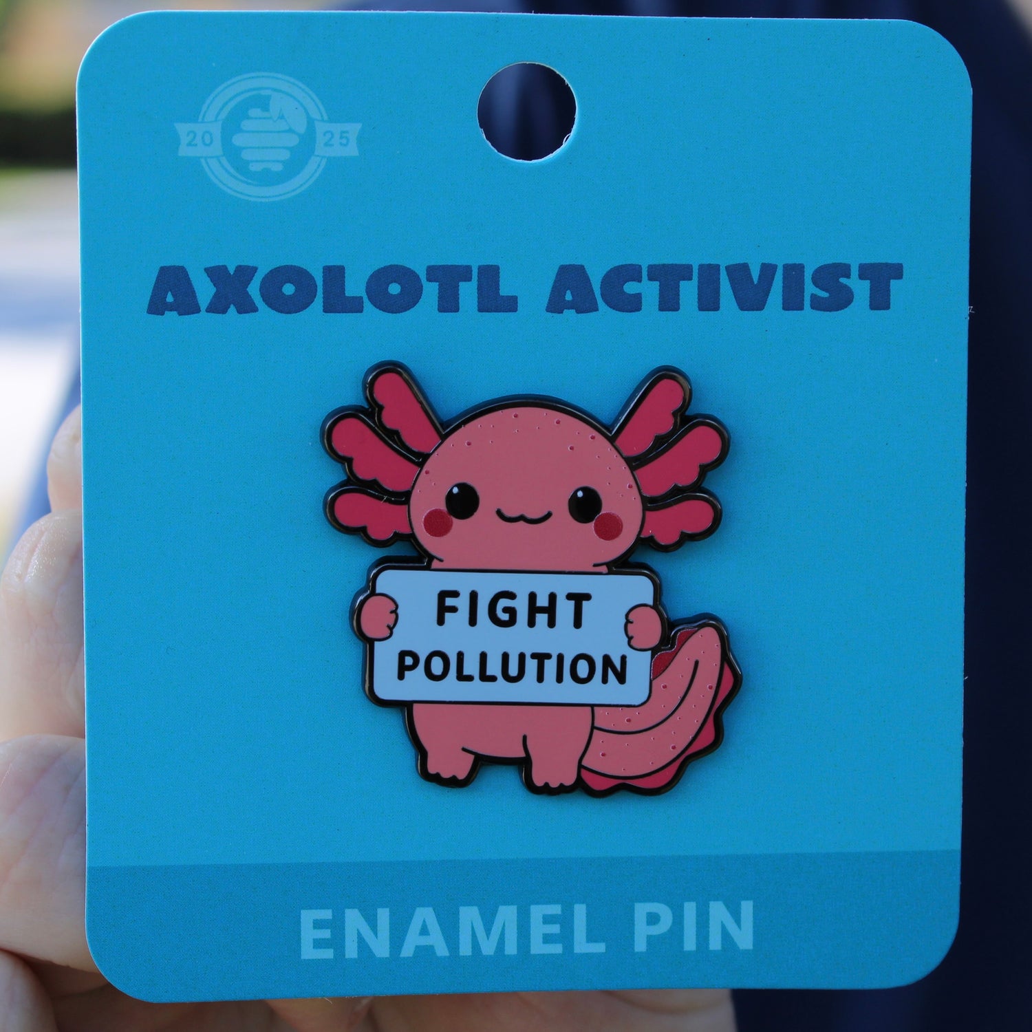 Axolotl enamel pin on a blue card with 'Fight Pollution' message