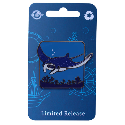 Manta ray enamel pin showing a navy and white manta gliding above coral on a blue eco backing card.