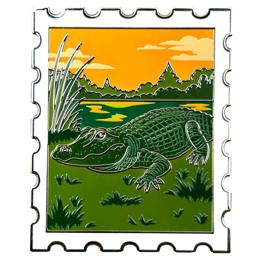 enamel pin shaped like a postage stamp featuring an american alligator at sunset in the everglades