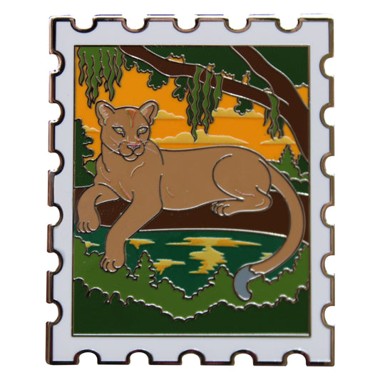 Enamel pin shaped like a postage stamp with a florida panther sitting on a branch at sunset 