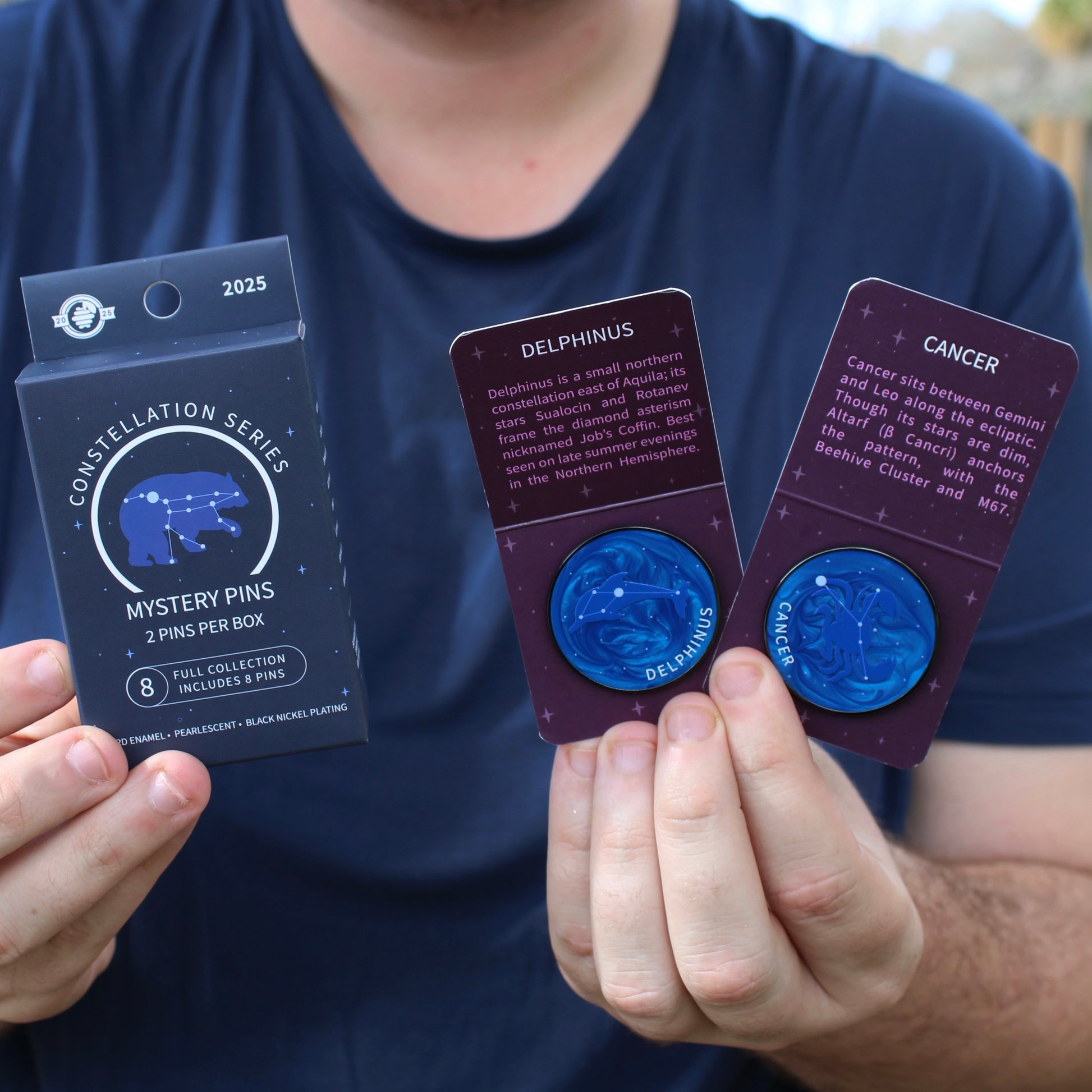 Person holding two constellation series mystery pins and a mystery box