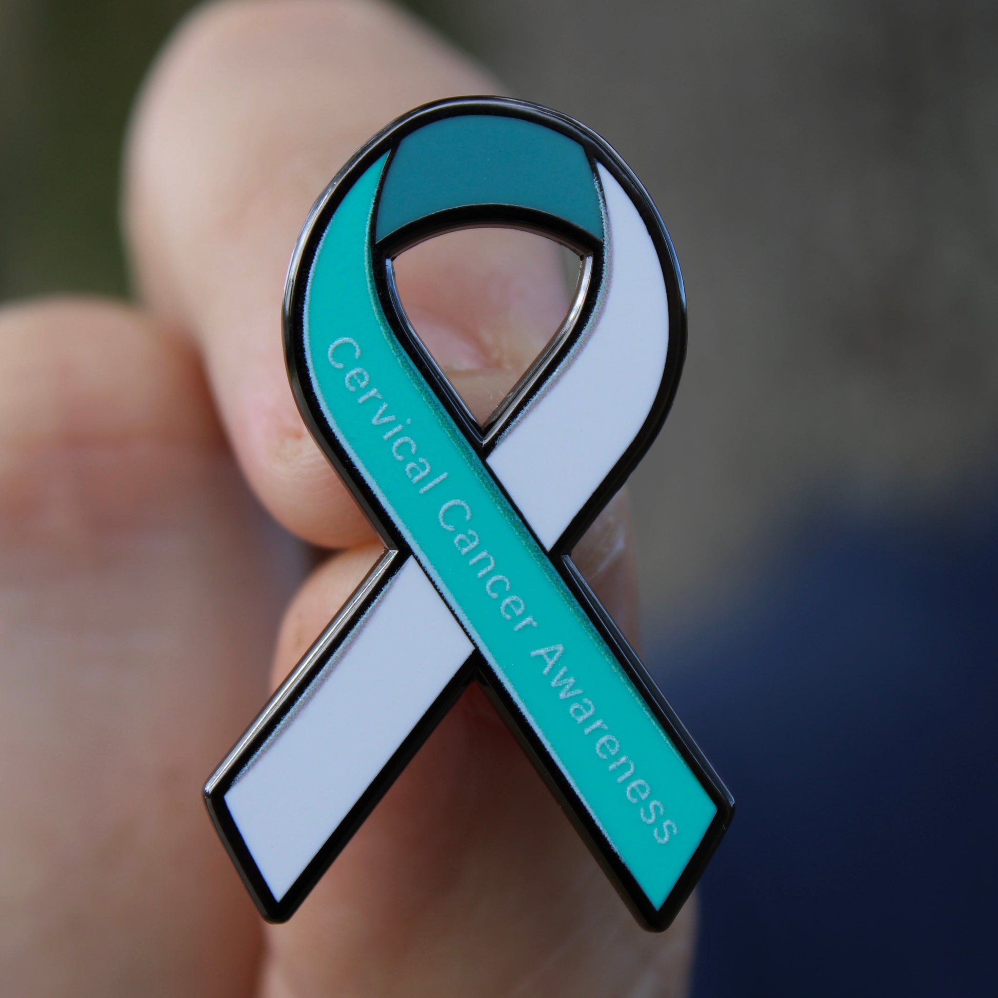 Close up of teal and white cervical cancer awareness ribbon enamel pin in hand