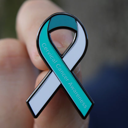 Close up of teal and white cervical cancer awareness ribbon enamel pin in hand